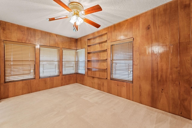 carpeted empty room with built in shelves, ceiling fan, a textured ceiling, and wooden walls