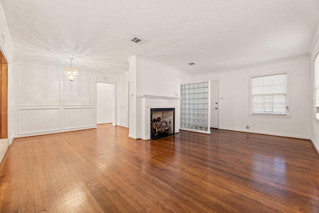 unfurnished living room featuring wood-type flooring, ornamental molding, a textured ceiling, and an inviting chandelier