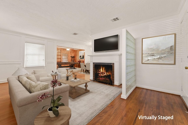 living room featuring a tile fireplace, crown molding, ceiling fan, a textured ceiling, and wood-type flooring