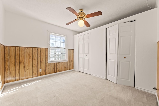 unfurnished bedroom featuring ceiling fan, wood walls, light carpet, and two closets