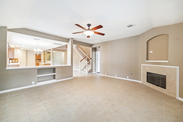 unfurnished living room with ceiling fan with notable chandelier, vaulted ceiling, built in shelves, light tile patterned floors, and a tiled fireplace