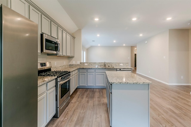 kitchen with kitchen peninsula, gray cabinets, appliances with stainless steel finishes, light hardwood / wood-style flooring, and sink