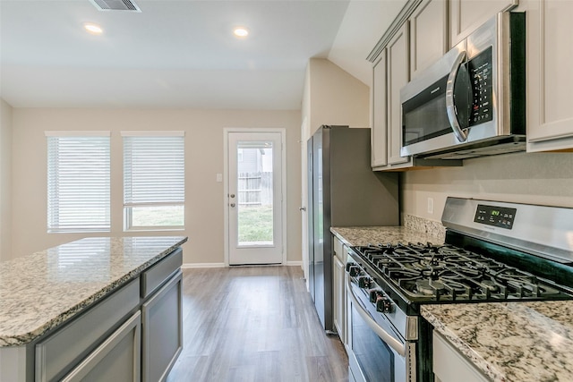 kitchen with lofted ceiling, gray cabinets, light stone counters, and stainless steel appliances