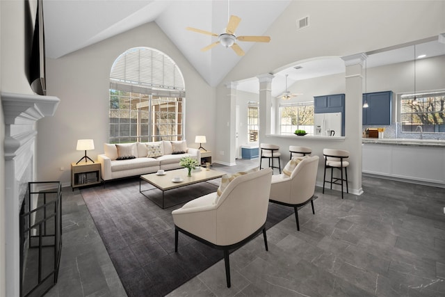 living room with decorative columns, a wealth of natural light, ceiling fan, and high vaulted ceiling