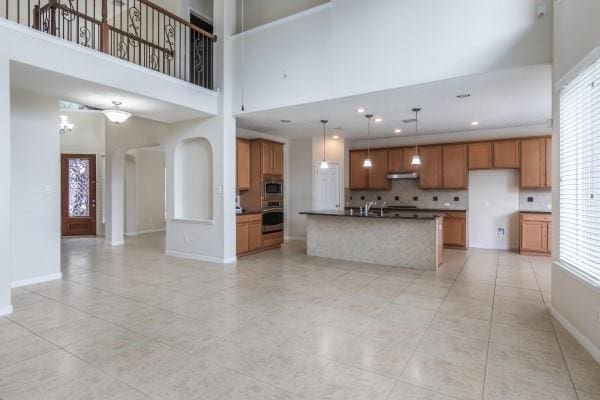 kitchen with a center island with sink, a towering ceiling, appliances with stainless steel finishes, tasteful backsplash, and light tile patterned flooring