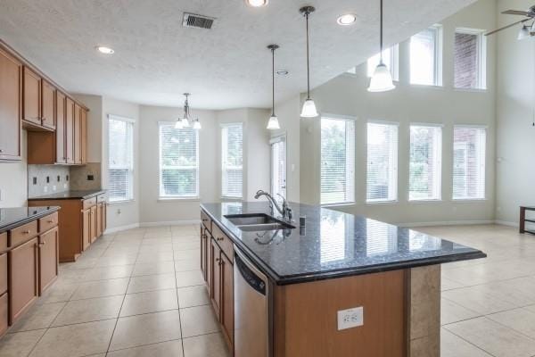 kitchen with stainless steel dishwasher, ceiling fan with notable chandelier, sink, pendant lighting, and an island with sink