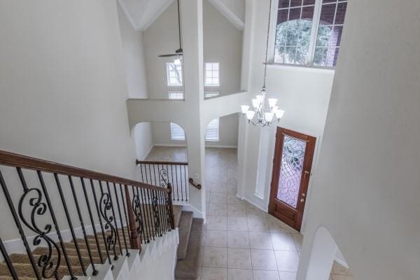 foyer entrance featuring plenty of natural light, a towering ceiling, ceiling fan with notable chandelier, and light tile patterned floors