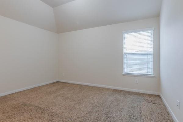 spare room featuring light colored carpet and vaulted ceiling