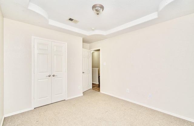 unfurnished bedroom featuring light carpet, a tray ceiling, and a closet