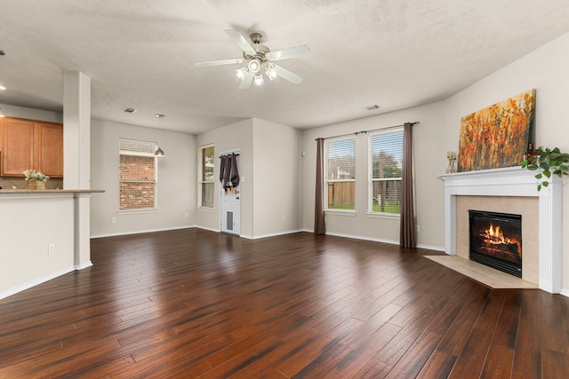 unfurnished living room with a tile fireplace, a textured ceiling, dark hardwood / wood-style floors, and ceiling fan