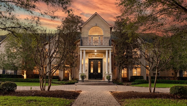 exterior entry at dusk featuring a lawn and a balcony