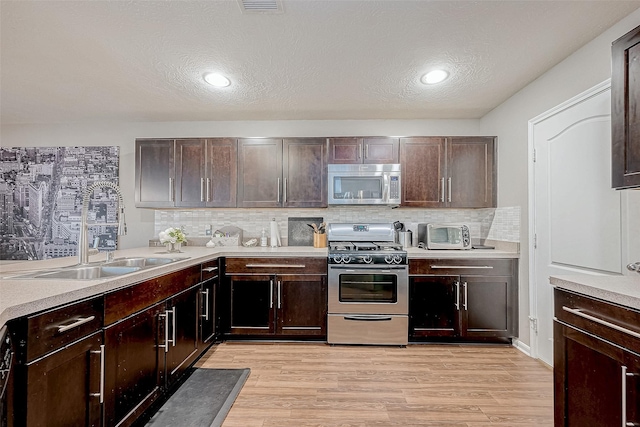 kitchen featuring decorative backsplash, light wood-type flooring, a textured ceiling, dark brown cabinets, and stainless steel appliances