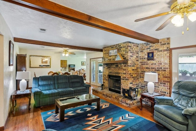 living room with beamed ceiling, wood-type flooring, a textured ceiling, and a brick fireplace