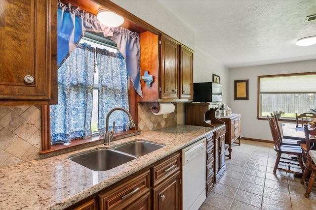 kitchen with backsplash, white dishwasher, sink, a healthy amount of sunlight, and light stone counters