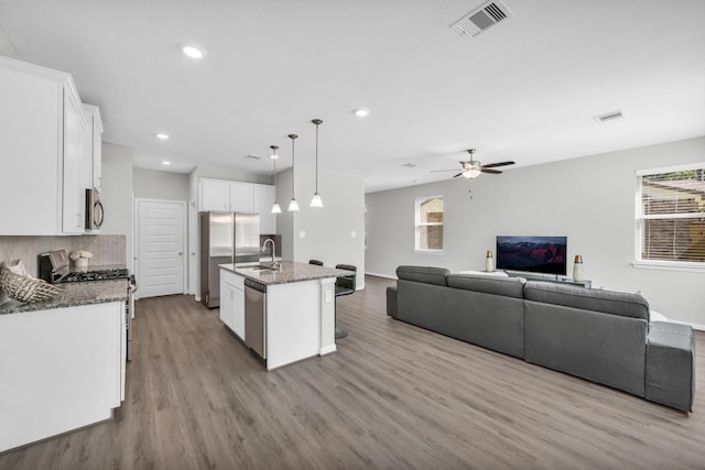 kitchen featuring appliances with stainless steel finishes, dark stone counters, decorative light fixtures, white cabinetry, and an island with sink