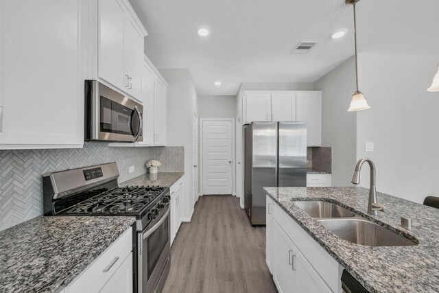 kitchen featuring dark stone counters, stainless steel appliances, sink, white cabinets, and hanging light fixtures