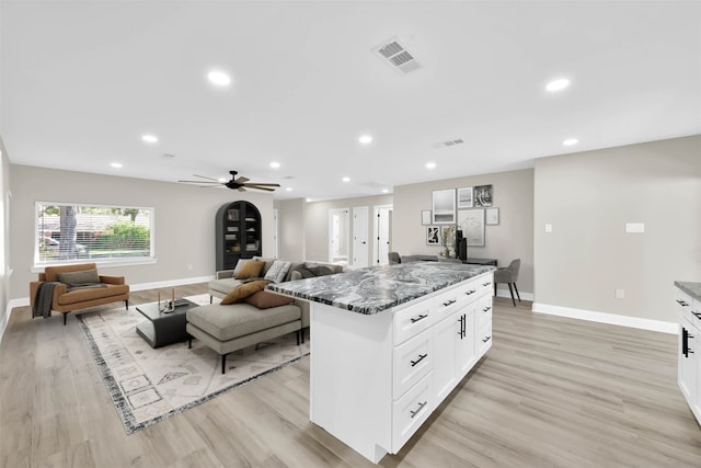 kitchen featuring white cabinetry, a center island, ceiling fan, dark stone countertops, and light wood-type flooring