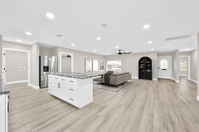 kitchen featuring white cabinetry, ceiling fan, a center island, stainless steel refrigerator with ice dispenser, and dark stone counters