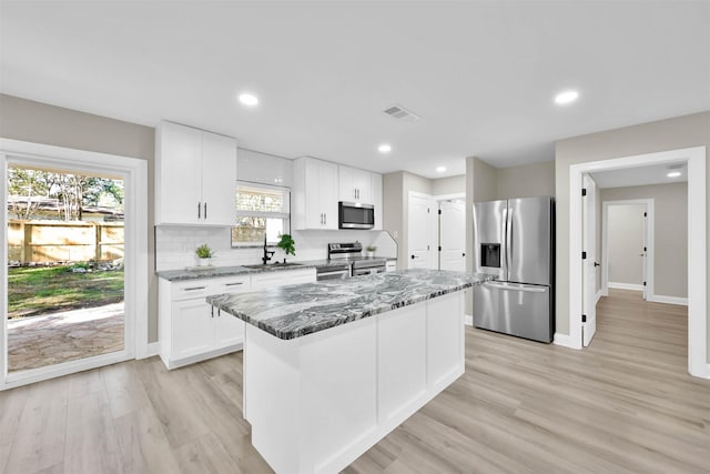 kitchen with dark stone counters, stainless steel appliances, sink, white cabinets, and a kitchen island