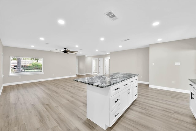 kitchen featuring a center island, dark stone counters, light hardwood / wood-style flooring, ceiling fan, and white cabinetry