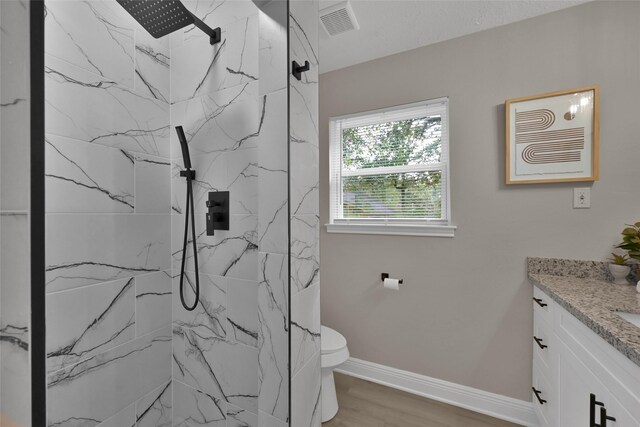 bathroom with tiled shower, wood-type flooring, vanity, and toilet