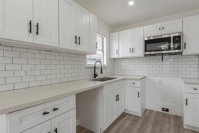 kitchen featuring stainless steel microwave, light wood-style flooring, decorative backsplash, a sink, and light stone countertops