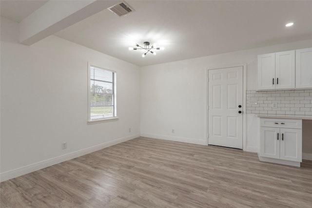 empty room featuring light hardwood / wood-style flooring, beamed ceiling, and a notable chandelier