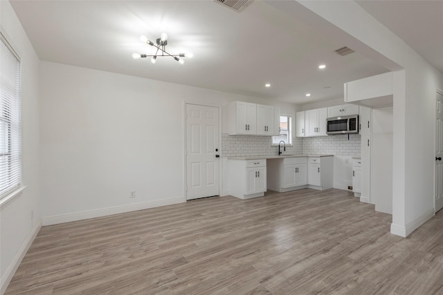 kitchen with tasteful backsplash, sink, an inviting chandelier, light hardwood / wood-style floors, and white cabinetry