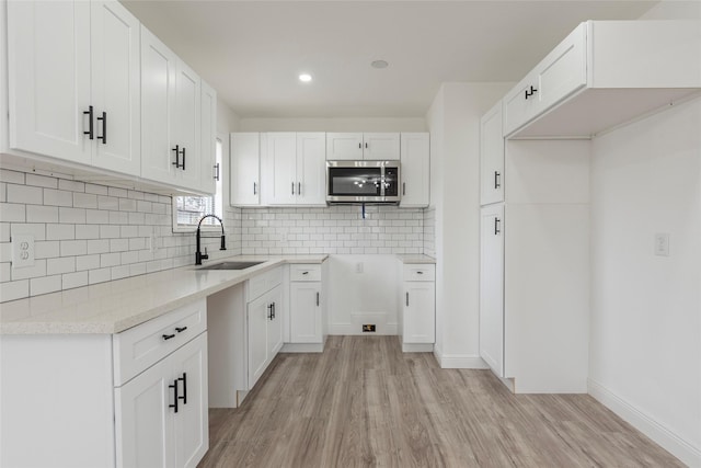 kitchen featuring light wood-type flooring, tasteful backsplash, white cabinetry, and sink