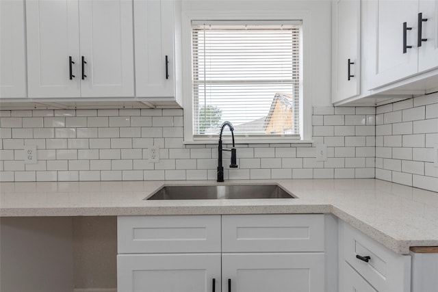 kitchen featuring backsplash, light stone counters, white cabinetry, and sink