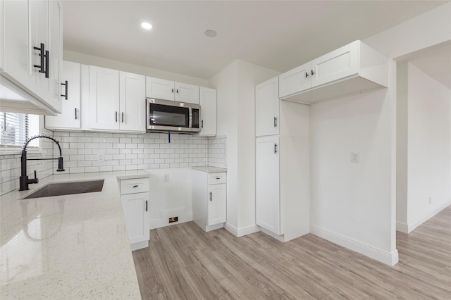 kitchen with white cabinetry, sink, light stone counters, decorative backsplash, and light wood-type flooring