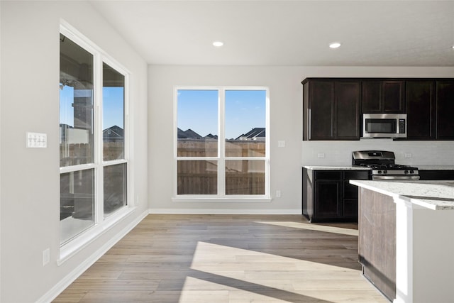 kitchen with light stone counters, stainless steel appliances, light hardwood / wood-style floors, and backsplash