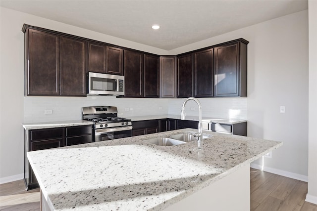 kitchen featuring stainless steel appliances, a center island with sink, light stone countertops, and sink