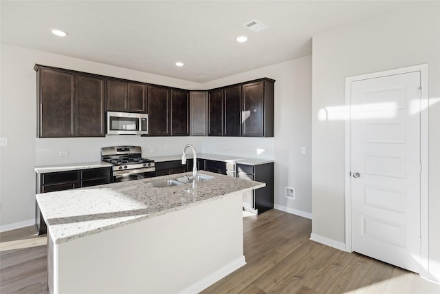 kitchen featuring a center island with sink, appliances with stainless steel finishes, light hardwood / wood-style floors, light stone countertops, and sink