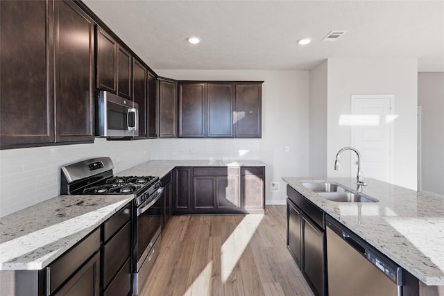 kitchen featuring light stone counters, stainless steel appliances, decorative backsplash, light wood-type flooring, and sink