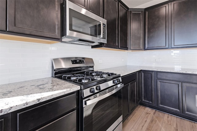 kitchen featuring appliances with stainless steel finishes, light hardwood / wood-style floors, light stone countertops, and dark brown cabinetry