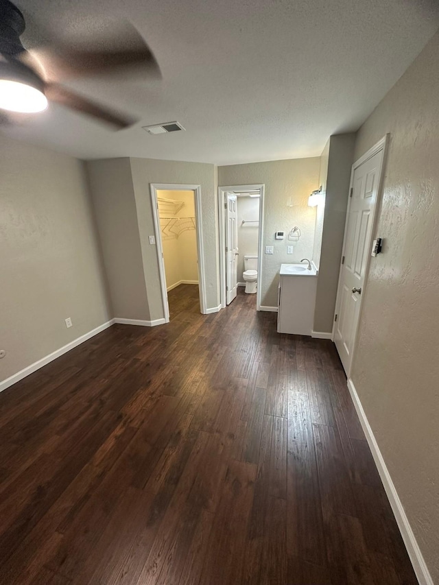 unfurnished bedroom with ceiling fan, dark wood-type flooring, ensuite bathroom, a walk in closet, and a closet