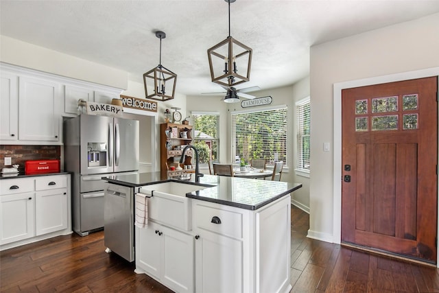 kitchen with stainless steel appliances, a center island with sink, decorative light fixtures, and white cabinetry