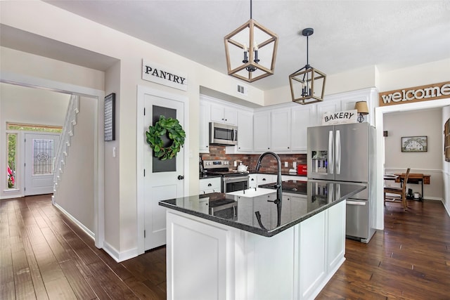 kitchen featuring stainless steel appliances, white cabinets, tasteful backsplash, hanging light fixtures, and a center island with sink