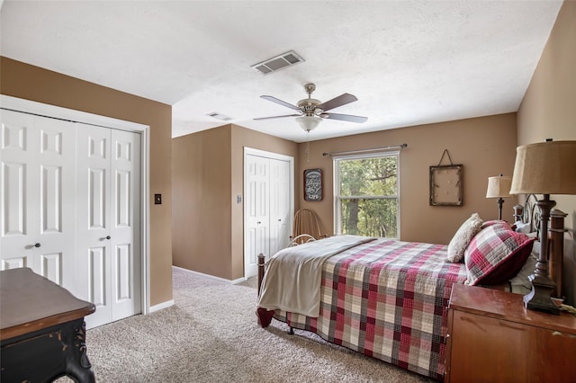 bedroom with ceiling fan, light carpet, and multiple closets