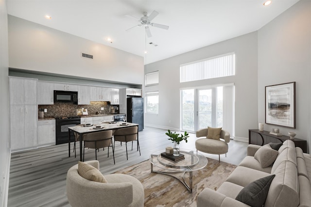 living room featuring ceiling fan, light hardwood / wood-style floors, and a high ceiling