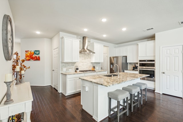 kitchen featuring sink, wall chimney exhaust hood, a center island with sink, white cabinets, and appliances with stainless steel finishes