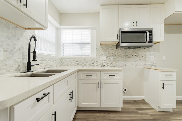 kitchen with light wood-type flooring, sink, tasteful backsplash, and white cabinets