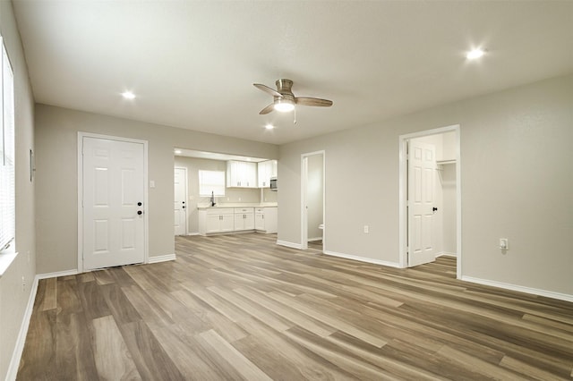 unfurnished living room with ceiling fan, light wood-type flooring, and sink