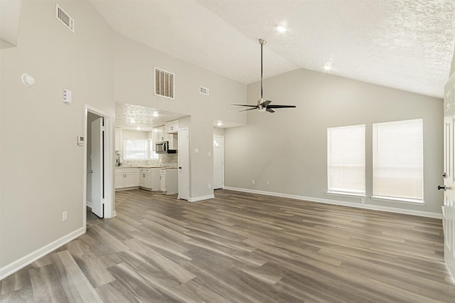 unfurnished living room featuring ceiling fan, high vaulted ceiling, light hardwood / wood-style floors, and a textured ceiling