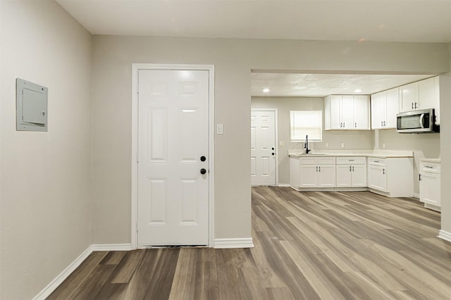 kitchen featuring electric panel, light hardwood / wood-style floors, white cabinetry, and sink