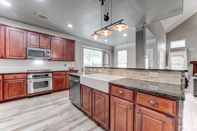 kitchen with appliances with stainless steel finishes, ornamental molding, a kitchen island with sink, hanging light fixtures, and lofted ceiling