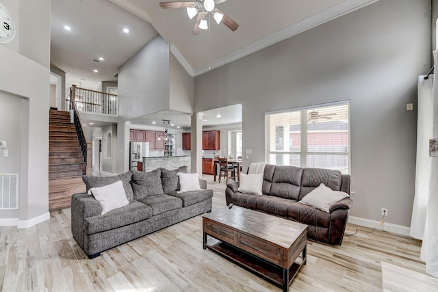 living room with crown molding, ceiling fan, a high ceiling, and light wood-type flooring