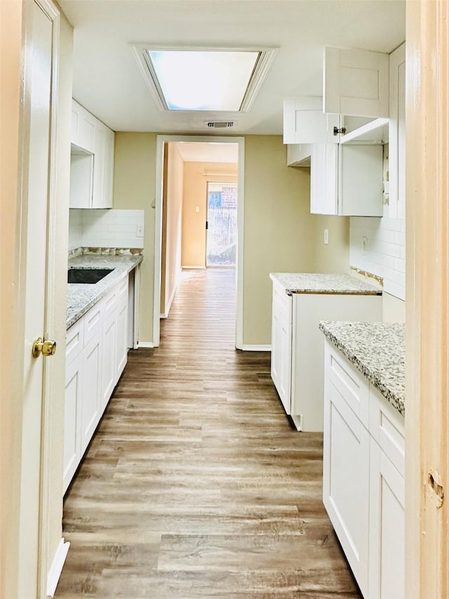 kitchen featuring white cabinets, light hardwood / wood-style floors, light stone countertops, and tasteful backsplash