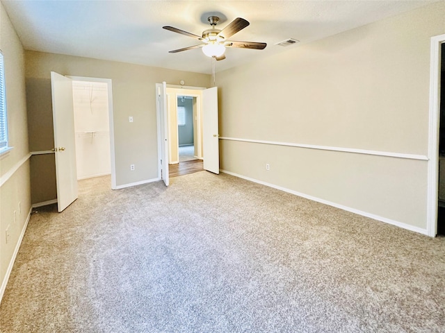 unfurnished bedroom featuring light carpet, a closet, a spacious closet, and ceiling fan